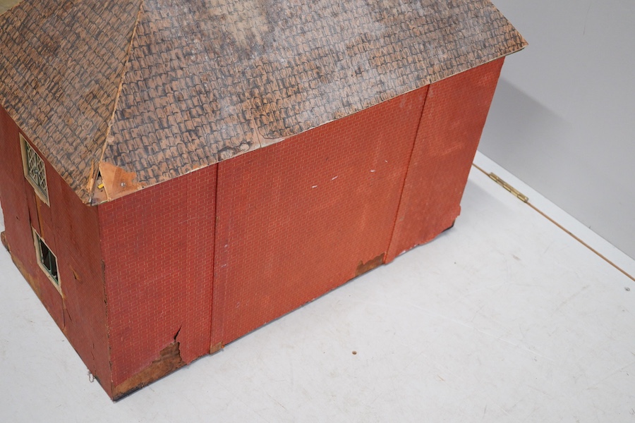 A 1920s/30s commercially produced dolls house, possibly by Tri-ang, of plywood construction, overlaid with printed paper roof tiles and brickwork, and tinplate windows and window frames, comprising of four rooms with bay